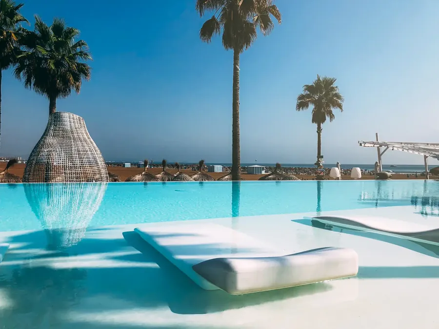 A resort pool on a beach lined with tall palms