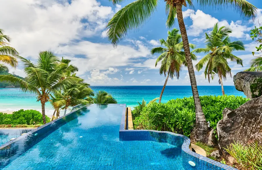 A resort pool under palms beside a white beach in the Seychelles