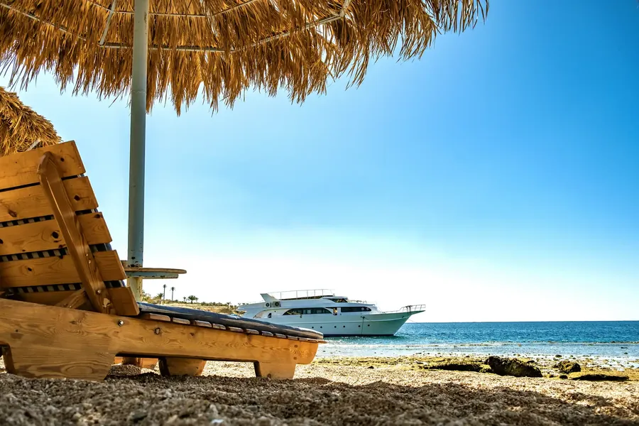 Wooden deck chairs under a straw umbrella on a white beach