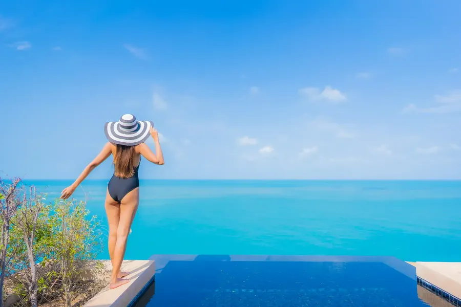 A woman in a striped sun hat looking out over a pool to the sea