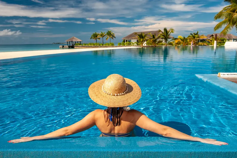 A woman in a straw hat in a pool facing a lagoon